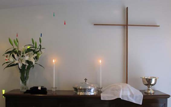 写真；礼拝堂の十字架と聖餐器・洗礼盤そして蝋燭と花